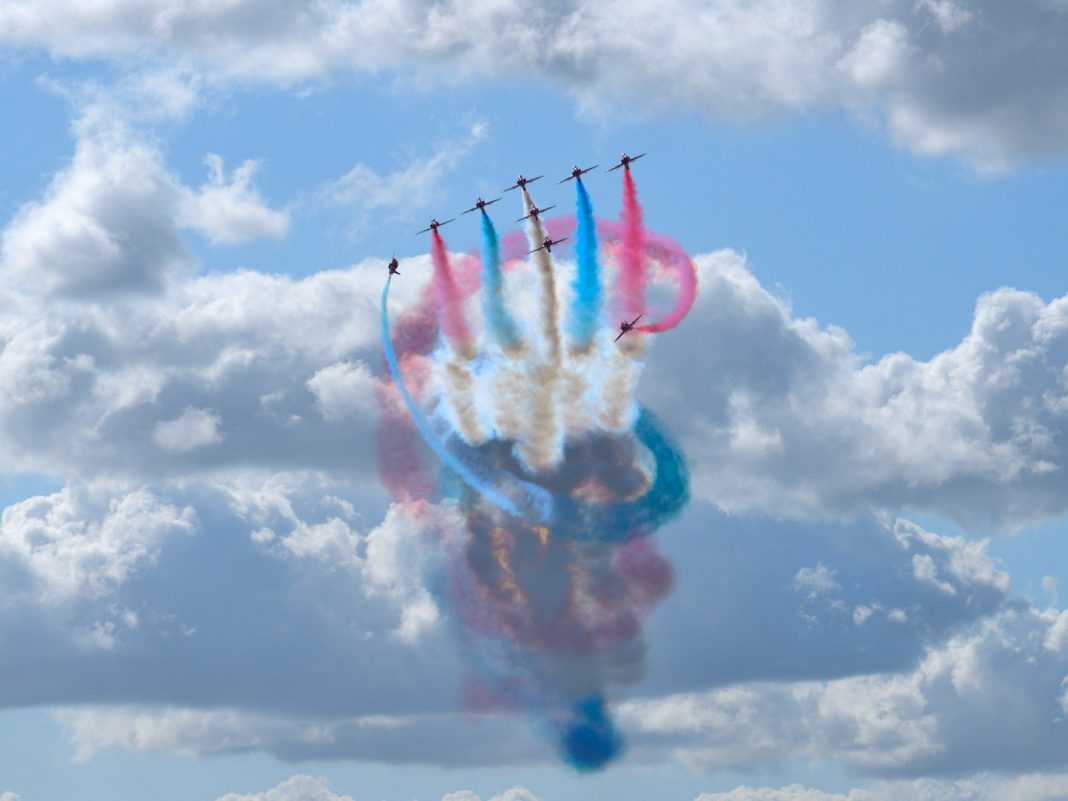 Planes perform aerobatics, leaving colorful smoke trails.