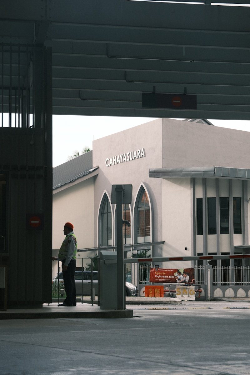 Security guard stands near building entrance with barrier gates.